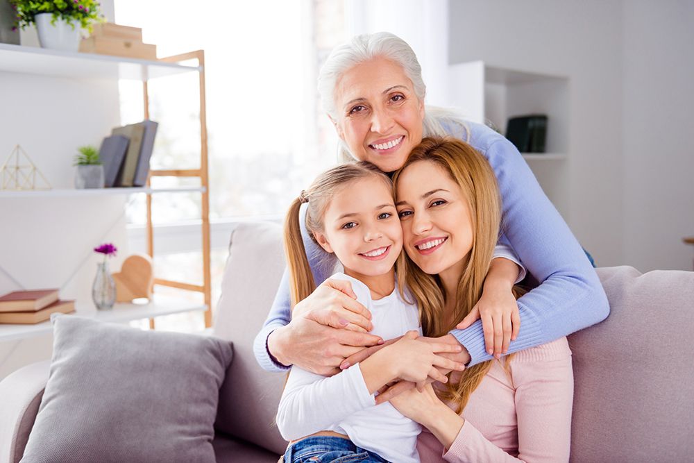 Portrait of three peaceful positive people cuddle sitting sofa toothy smile look camera house indoors